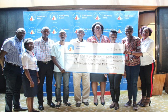 Beatrice Lugalambi (4th R), Centenary Bank’s General Manager, Corporate Communication & Marketing hands over a dummy cheque worth UGX 4 million to its customers and staff as a reward for transacting using their Cente Visa card across the different digital platforms at least 4 times a week under the 'Kwasa with CenteVisa' promotion.